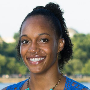 Photograph of a Black woman with natural curls hair smiling at the camera