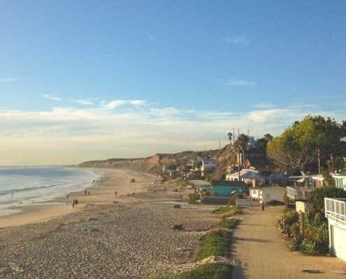 A wide beach during the golden hour just before sunset, with houses in the foreground and cliffs stretching away to the north