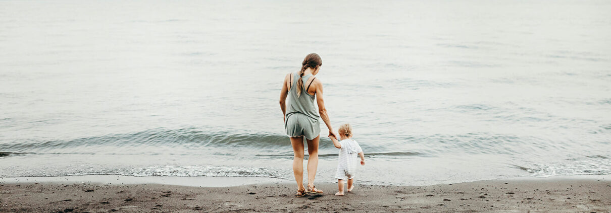 A woman and child walk on a beach towards the ocean