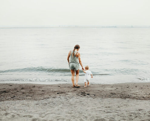 A woman and child walk on a beach towards the ocean