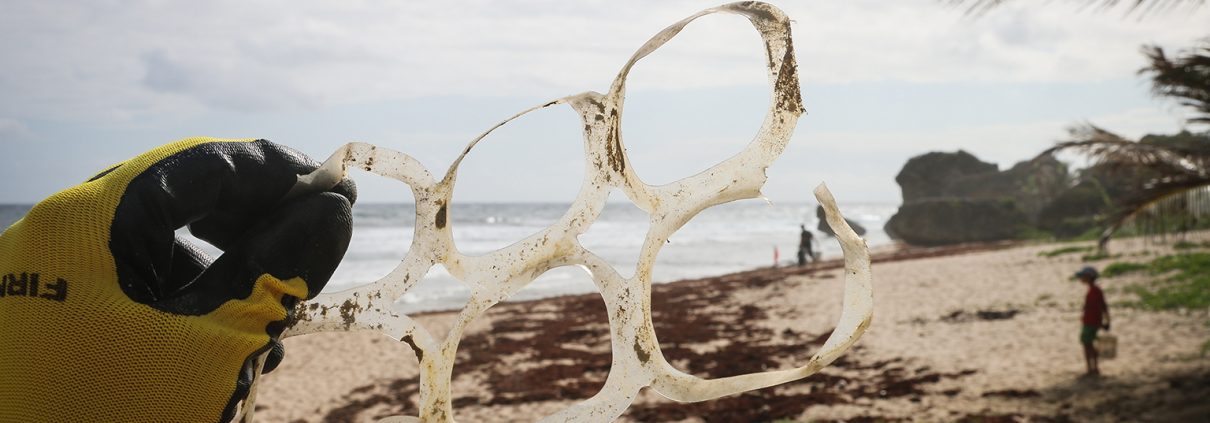 Gloved hand holding a set of dirty plastic pack rings on a cloudy beach