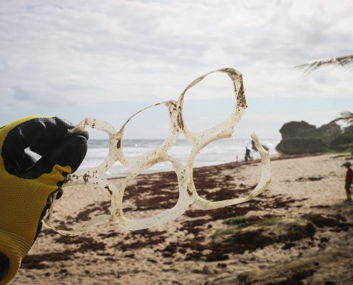 Gloved hand holding a set of dirty plastic pack rings on a cloudy beach