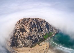 Aerial photo of Morro Rock and the parking lot for Morro Bay surrounded by fog