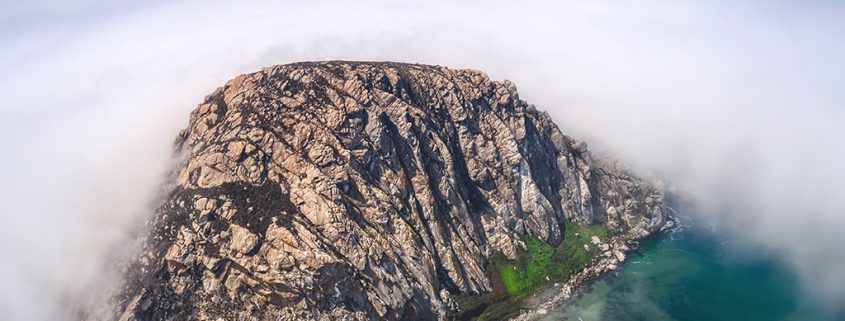 Aerial photo of Morro Rock and the parking lot for Morro Bay surrounded by fog