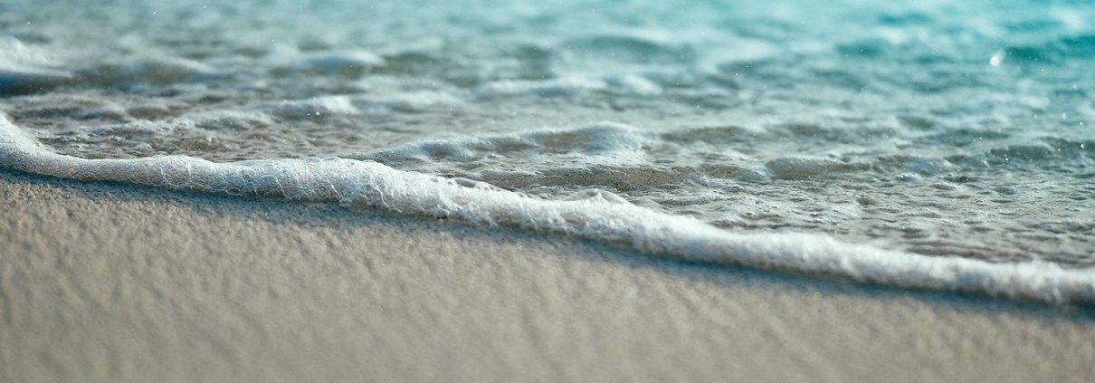 A close-up photo of sea foam on a white sand beach