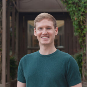 Photograph of a young blond man in a green shirt smiling at the camera