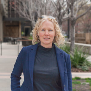 Photograph of a blonde woman in a navy blazer looking at the camera