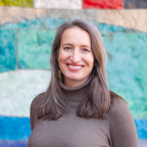 Photograph of a brunette woman in a brown turtleneck smiling at the camera