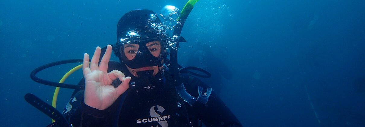Photograph of a young woman making the OK gesture while SCUBA diving