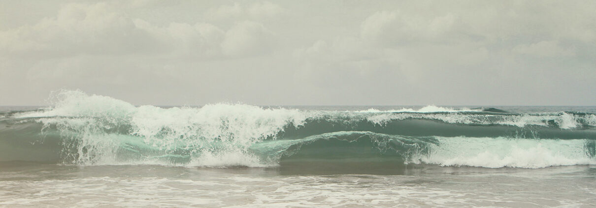 Photograph of muted gray-green waves crashing on a beach