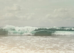 Photograph of muted gray-green waves crashing on a beach