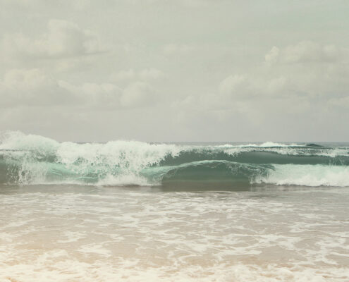 Photograph of muted gray-green waves crashing on a beach