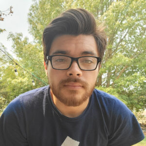 A young Latinx man wearing glasses smiles slightly at the camera.