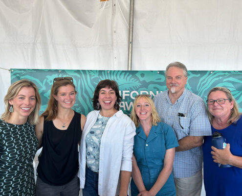 Six people smile at the camera, standing in front of a mostly-hidden banner of seaweed and a white pavilion wall.