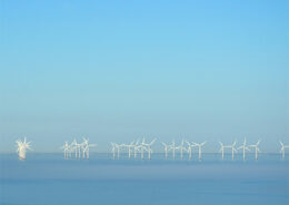 A distant line of offshore wind turbines on a blue and cloudless day